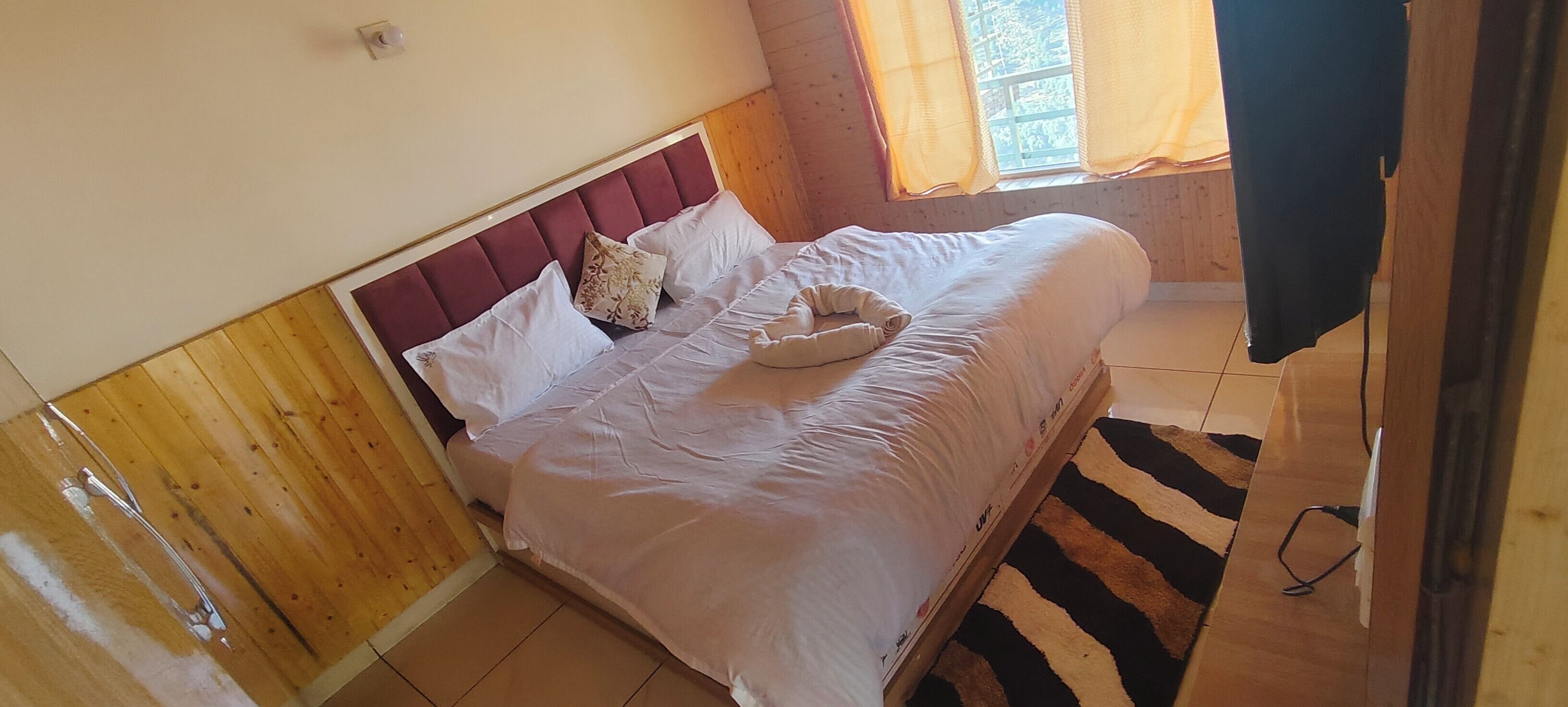 Une chambre à coucher avec une tête de lit en bois, un lit avec une literie blanche et une fenêtre avec des rideaux.