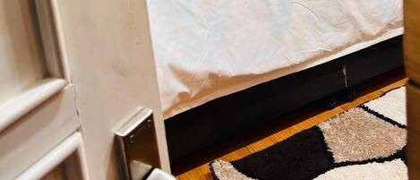 A bedroom with a bed, a headboard, a nightstand, a wall-mounted lamp, and a patterned rug.