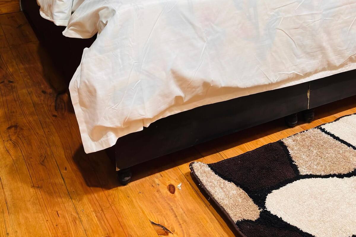 Una cama con cabecera oscura, ropa de cama blanca y almohadones decorativos.