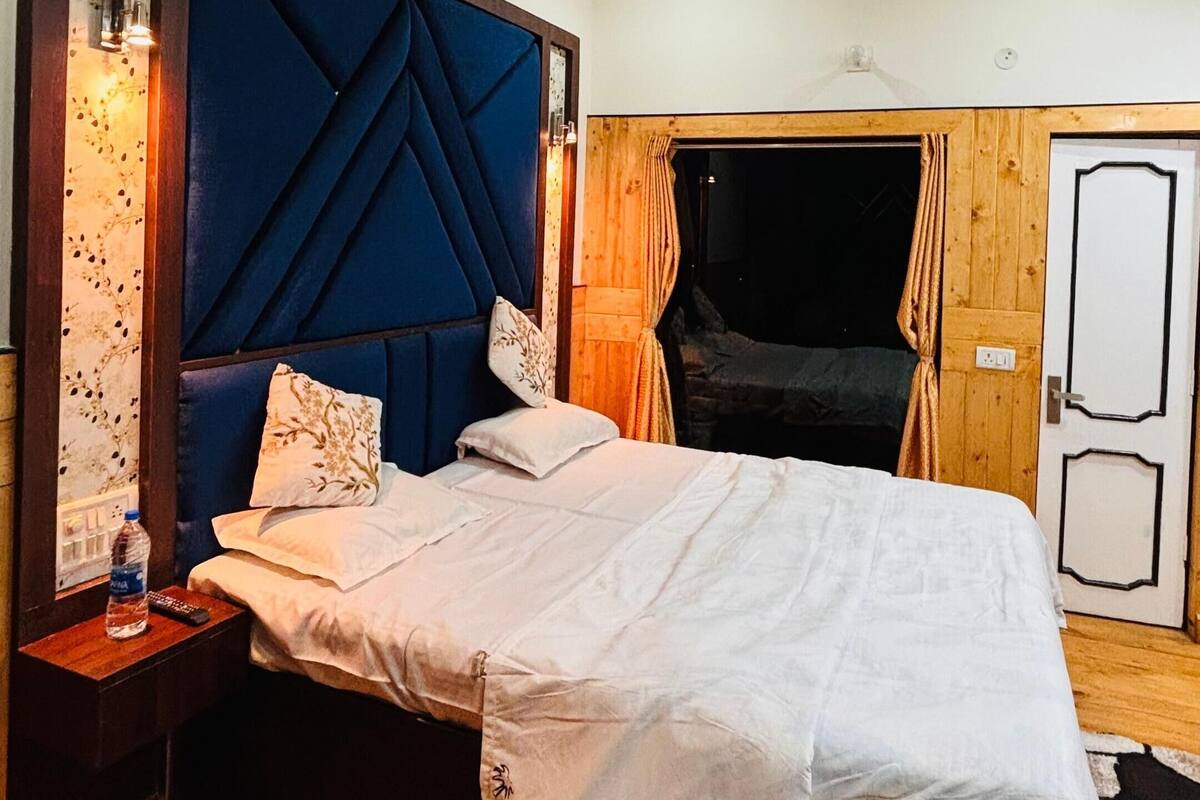 Un dormitorio con cama, ventilador de techo, mesita de noche, botella de agua y una puerta.