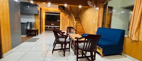 A dining area with wooden chairs and a table, a blue sofa, and a staircase leading to an upper level.