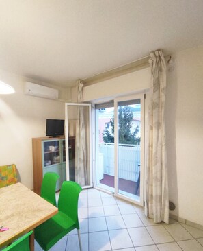 A room with a dining table, chairs, a TV, and a sliding glass door leading to a balcony. - Bright and Comfortable Flat (San Michele al Tagliamento)