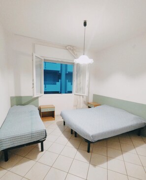 A room with two single beds, a window with a view, a hanging light fixture, and a small wooden nightstand. - Bright and Comfortable Flat (San Michele al Tagliamento)