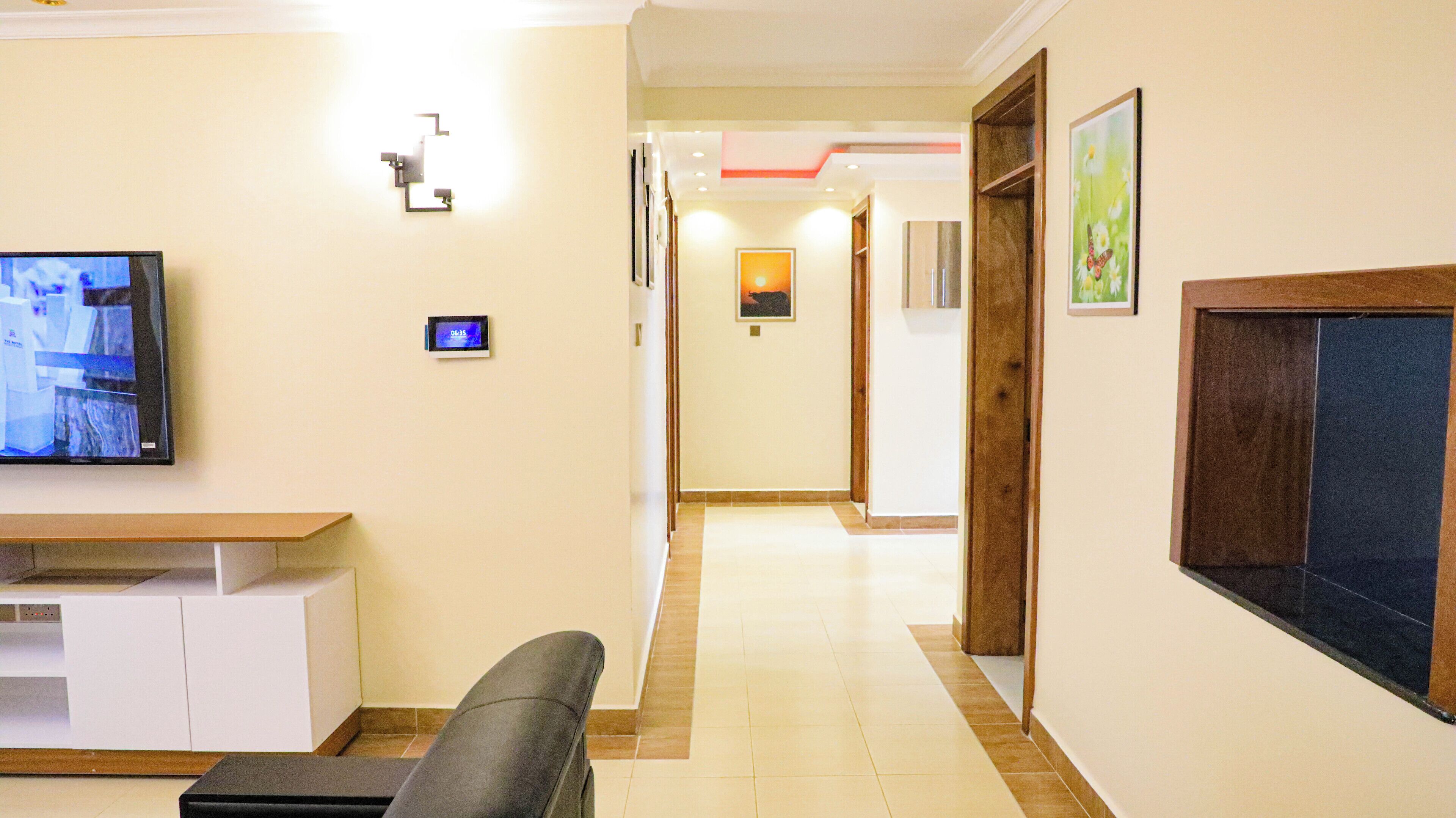 Un pasillo de hotel con una mesa de recepción, un televisor, un reloj digital y obras de arte enmarcadas en las paredes.
