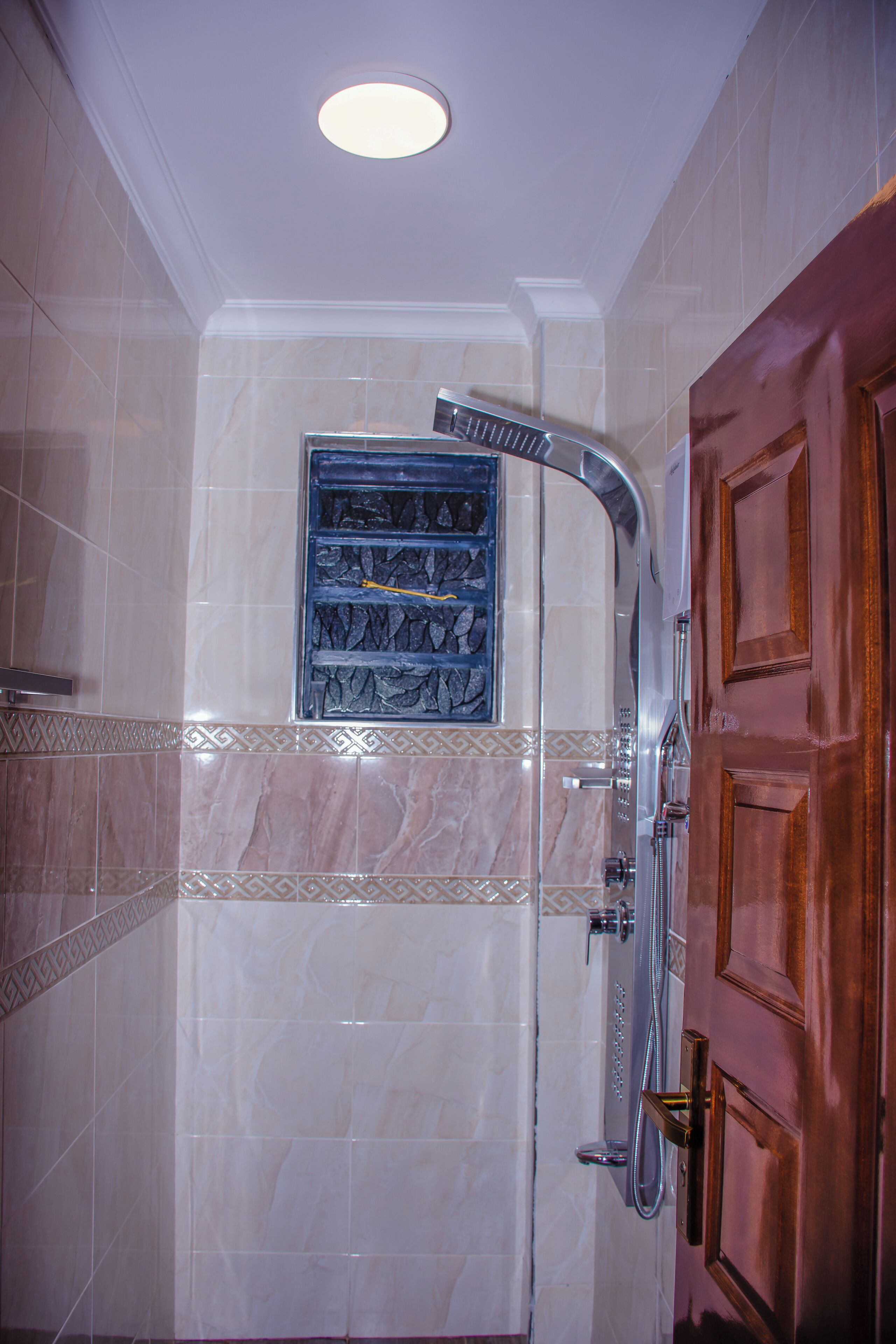 Une salle de bain avec une douche, une porte en bois et un mur carrelé agrémenté d’une bordure décorative.