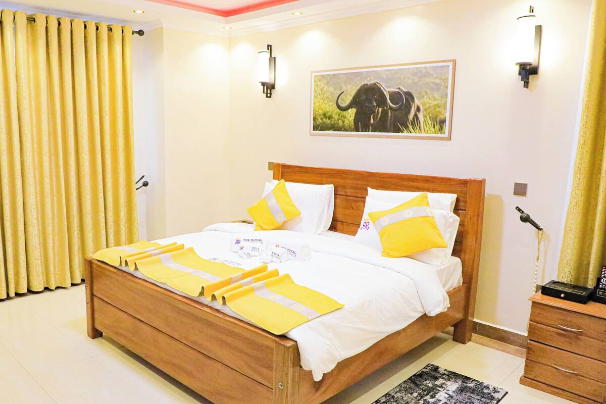 A neatly made bed with a wooden frame, white and yellow bedding, and a picture of an elephant on the wall.