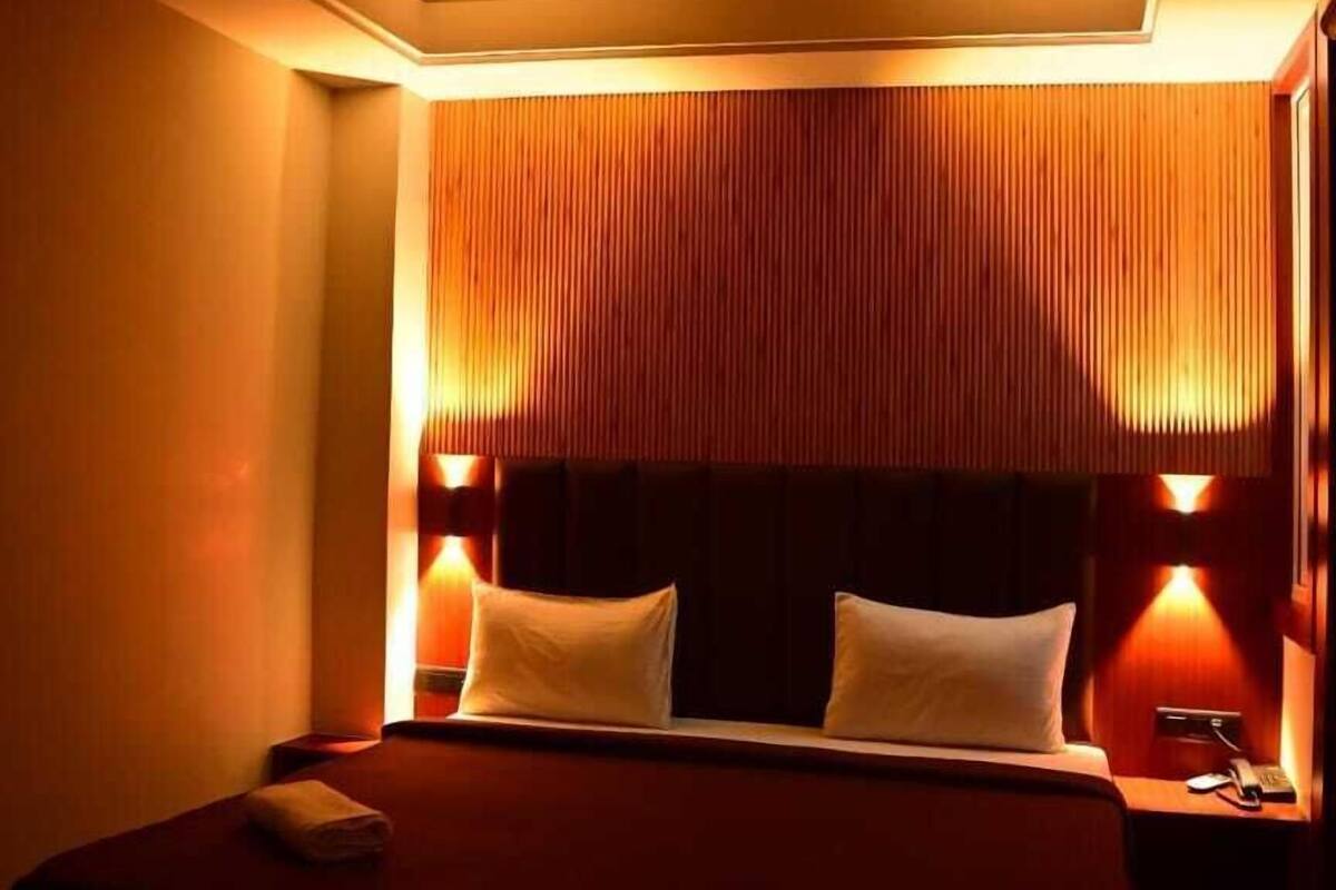 A dimly lit hotel room with a bed, a ceiling fan, and wall-mounted lamps.