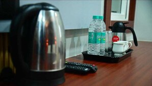 A coffee maker, two water bottles, a cup, and a remote control on a tray. - Hotel Baba Vishwanath Palace  (Prayagraj)