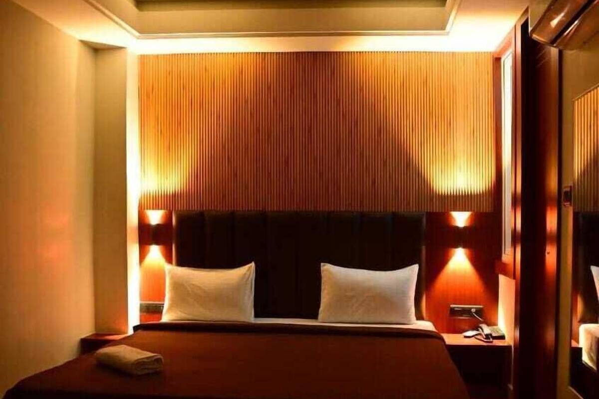 A hotel room with a large bed, two bedside lamps, a ceiling fan, and a nightstand with a phone.