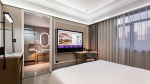 Egy modern szállodai szoba, amelyben egy nagy ágy, egy íróasztal, a falra szerelt televízió és egy fürdőszoba található, mely utóbbi egy nyitott ajtón keresztül belátható.