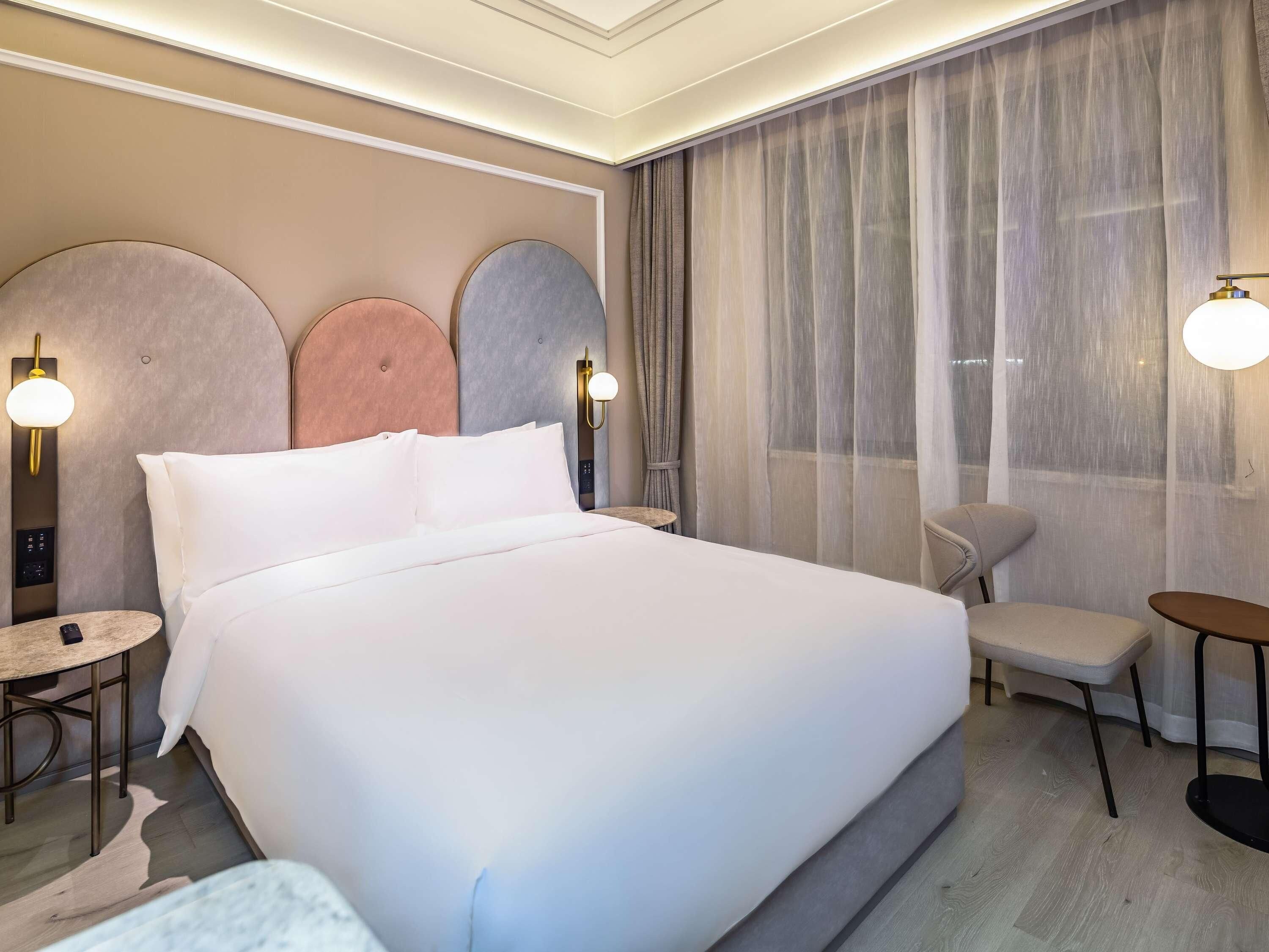A hotel room with a large bed, a small round table, a chair, and a desk.