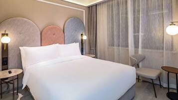A hotel room with a large bed, a small round table, a chair, and a desk.