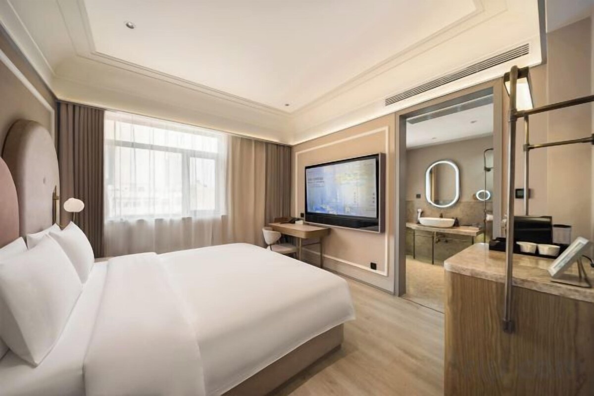Une chambre d’hôtel comprenant un grand lit, une télévision, un bureau avec une chaise, une salle de bain avec un lavabo et un miroir.