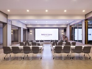 A conference room with a large screen displaying 'Mercure Hotels' branding, equipped with multiple tables and chairs. - Mercure Qingdao Zhanqiao (Qingdao)