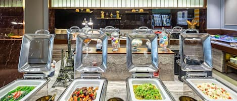 A buffet area with various food stations, including a salad bar, a meat station, and a pasta station, all with clear signage.