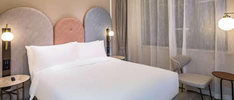 Ein Hotelzimmer mit einem großen Bett, einem kleinen runden Tisch, einem Stuhl und einem Schreibtisch.