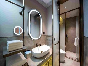 Un baño moderno con un espejo ovalado grande, un espejo redondo, un lavamanos blanco y una ducha con mampara de vidrio.