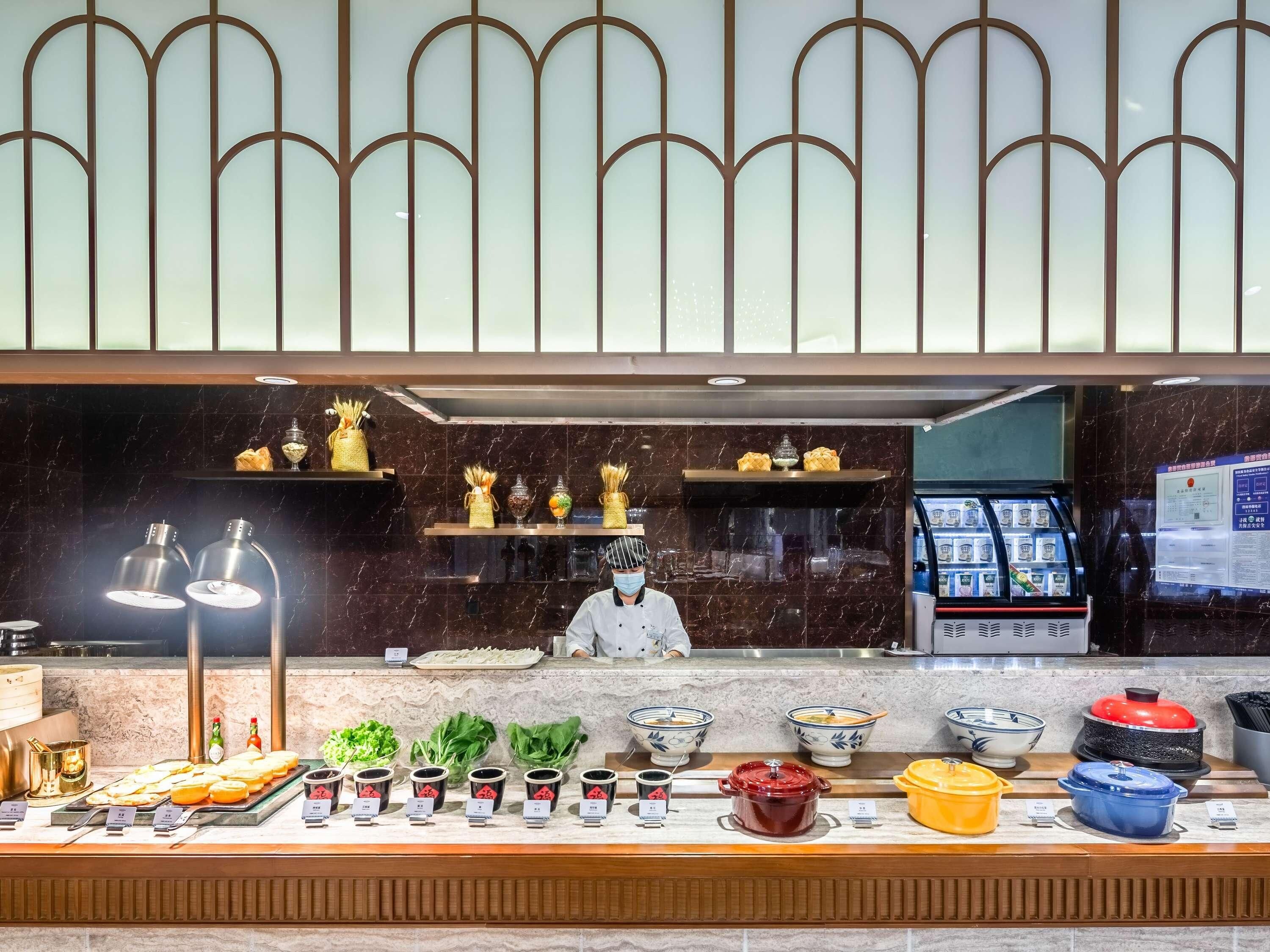 Een buffetgedeelte met diverse gerechten en bijbehorende sauzen, een kok in uniform en een gekoelde vitrine.