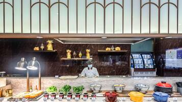 Een buffetgedeelte met diverse gerechten en bijbehorende sauzen, een kok in uniform en een gekoelde vitrine.