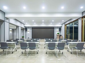 Una sala de conferencias moderna con una pantalla grande, varias mesas y sillas.