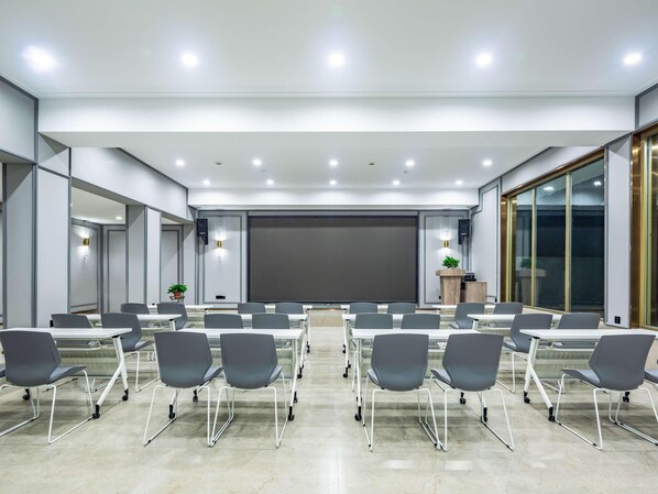 A modern conference room with a large screen, multiple tables, and chairs. - Mercure Qingdao Zhanqiao (Qingdao)