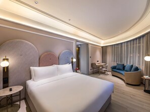 A modern hotel room with a large bed, a seating area with a sofa and chairs, a small table, and a separate dining area. - Mercure Qingdao Zhanqiao (Qingdao)