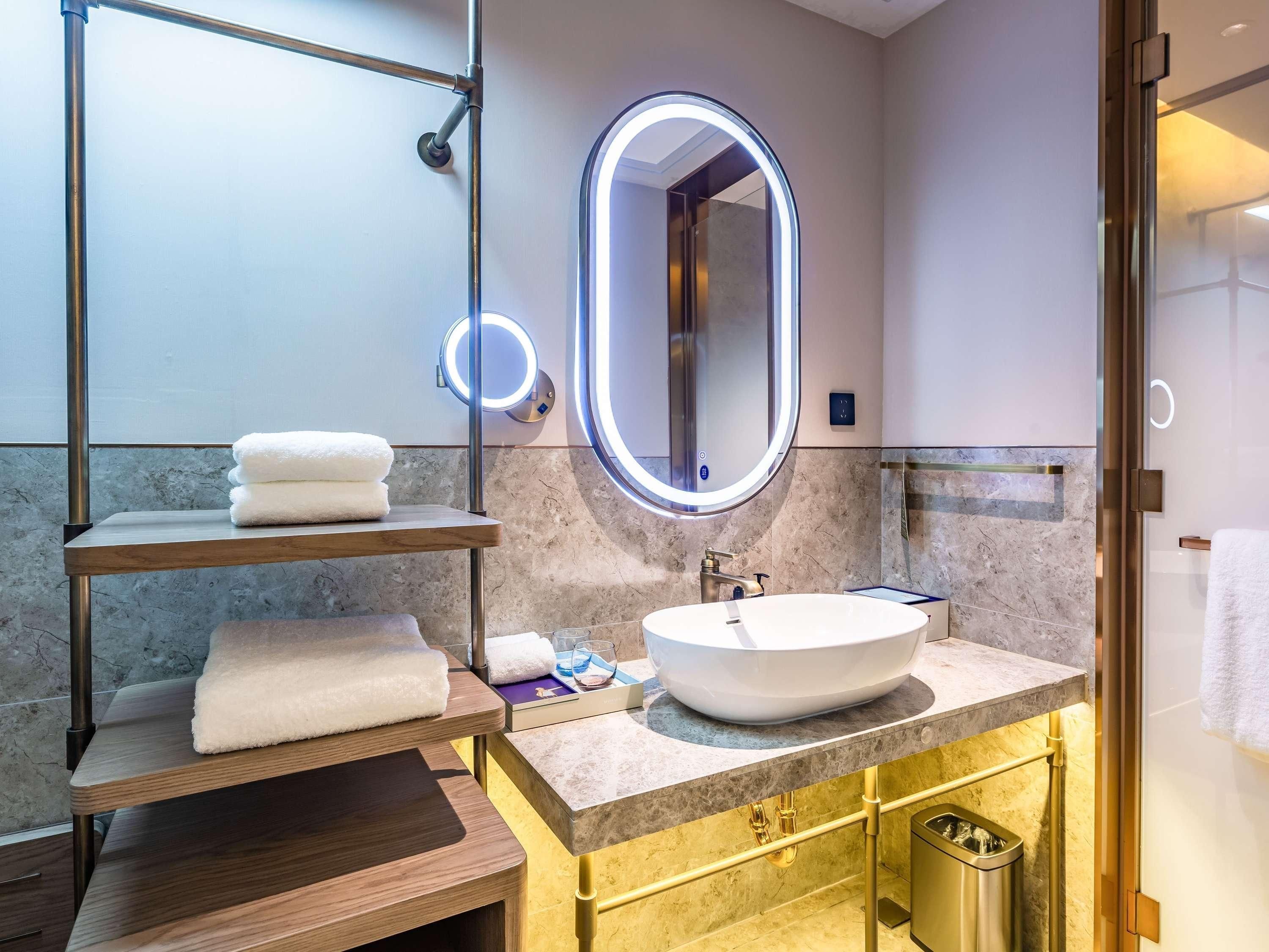Un baño moderno con un espejo redondo, un lavamanos blanco y paredes de mármol.