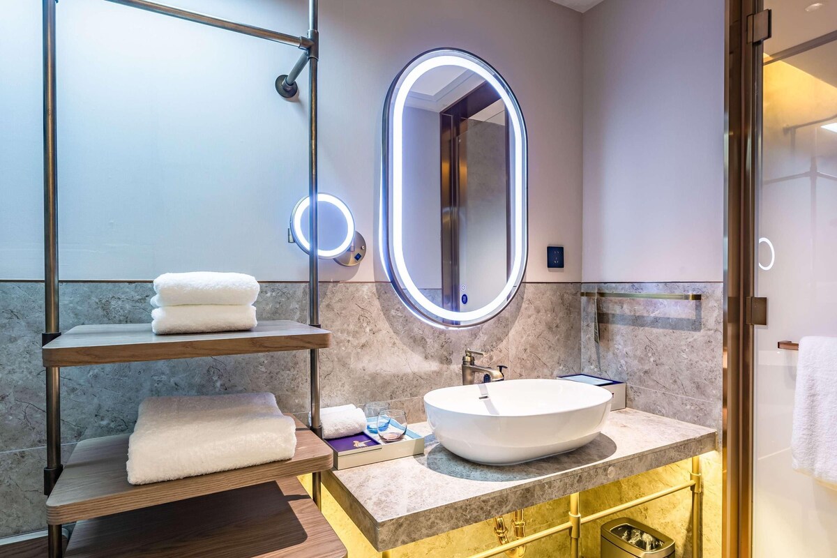 A modern bathroom with a round mirror, a white sink, and marble walls.