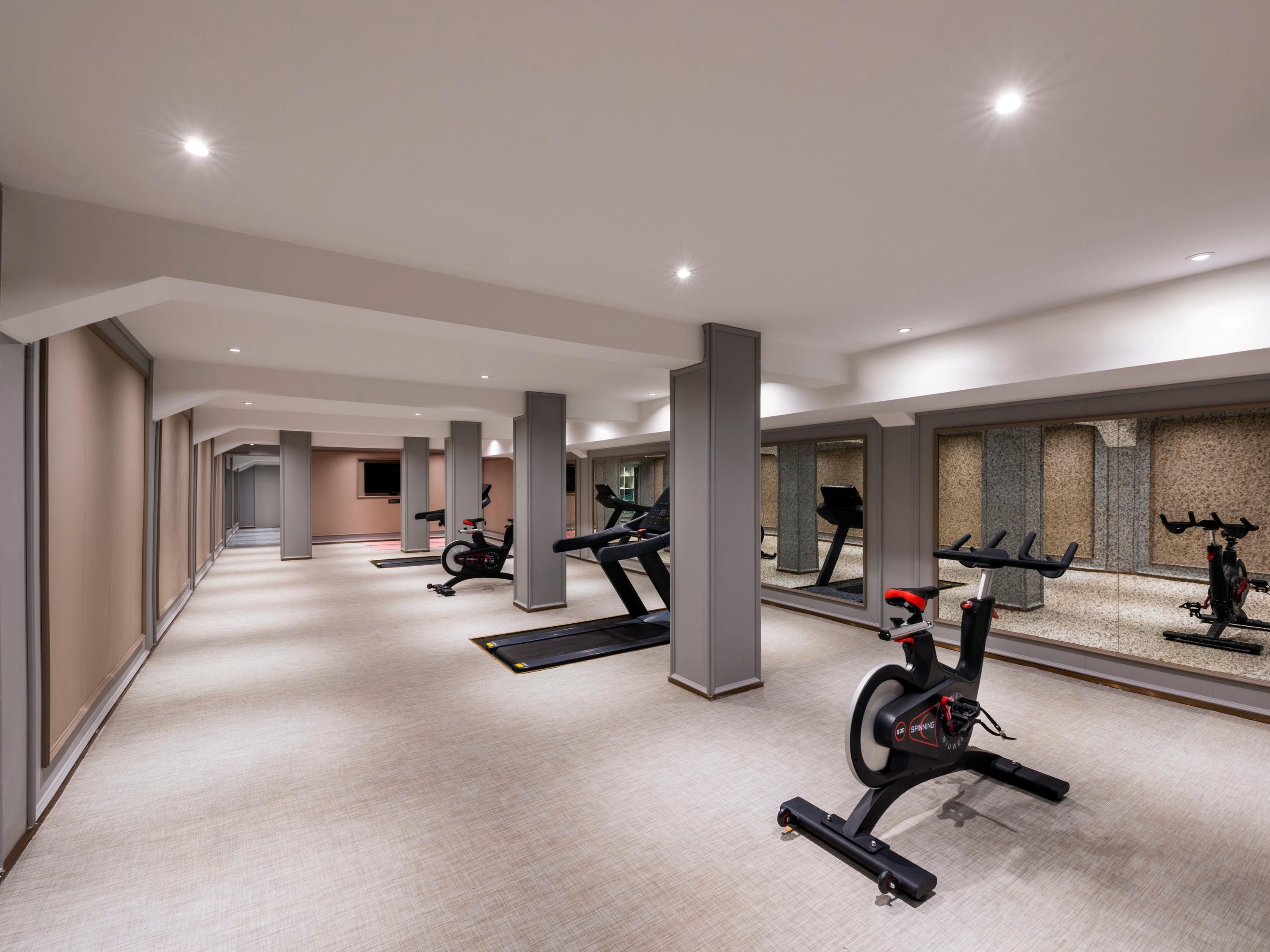 A modern gym with multiple exercise machines, a long corridor, and a mirrored wall.