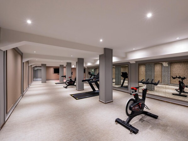 Un gimnasio moderno con varias máquinas de ejercicio, un largo pasillo y un muro con espejos.