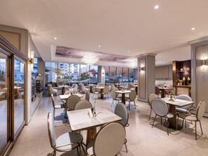 A modern restaurant with multiple dining tables and chairs, large windows offering city views, and elegant lighting fixtures. - Mercure Qingdao Zhanqiao (Qingdao)