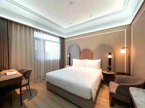Una habitación de hotel moderna con una cama grande, un escritorio, dos sillas y una mesita de noche con lámpara.