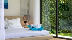 A bedroom with a bed, a nightstand, a lamp, and a view of greenery through a large window. - Bali Style Pool Villa - Private & Serene (Choeng Mon)