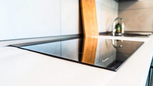 A modern kitchen with a sleek black induction cooktop, a wooden panel, and a stainless steel faucet. - Renovated Holiday Home With Pool in Bibione (San Michele al Tagliamento)