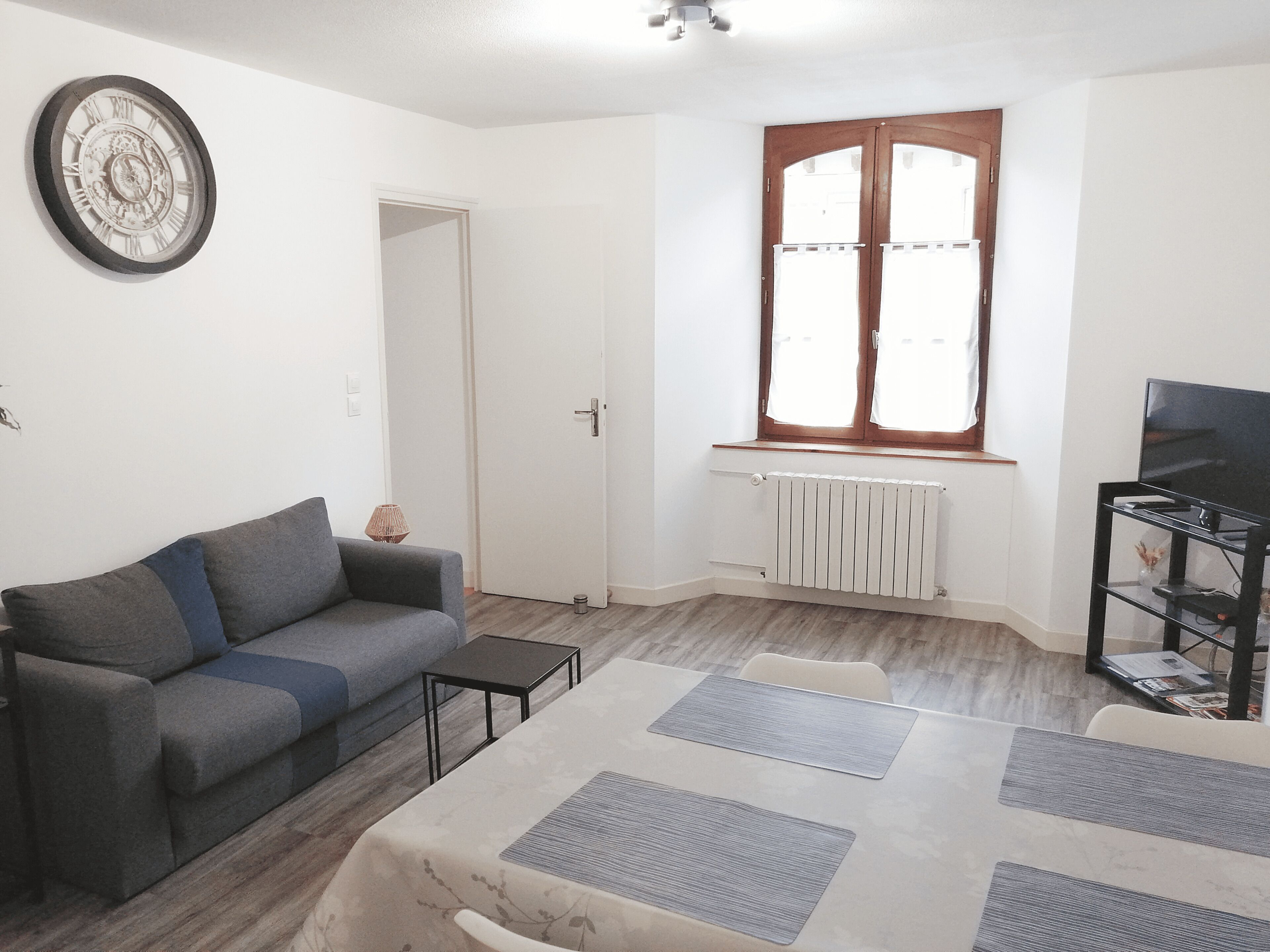 A living room with a grey sofa, a small table, a radiator, and a TV stand.