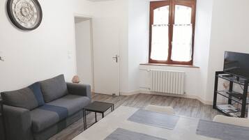 A living room with a grey sofa, a small table, a radiator, and a TV stand.