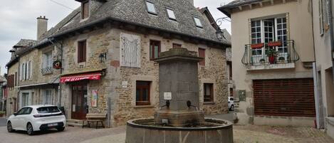 A stone building with a fountain in the center, a parked car, and a sign for a restaurant.
