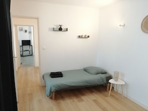 Un dormitorio pequeño y ordenado, con una cama, una mesita de noche y un estante en la pared con una planta.