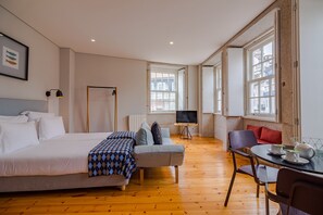 A hotel room with a bed, a sofa, a TV, a dining table, and large windows. - Pretty Apartment With Modern Comforts (Porto)