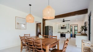 Un vaste espace dédié à la salle à manger, avec une table et des chaises en bois, un luminaire suspendu et une vue sur la cuisine.