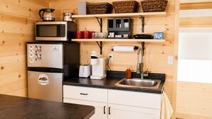 A compact kitchen with a microwave, toaster, and refrigerator, wooden walls, and a wooden countertop. - Private Tiny Cabin in Glendive Near Makoshika Park - Free Parking & WiFi (Glendive)