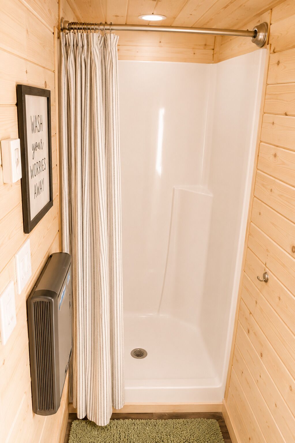 A wooden cabin bathroom with a shower, a framed sign, and a heater.