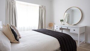 Un dormitorio con una cama, un tocador blanco, un espejo redondo y una silla.