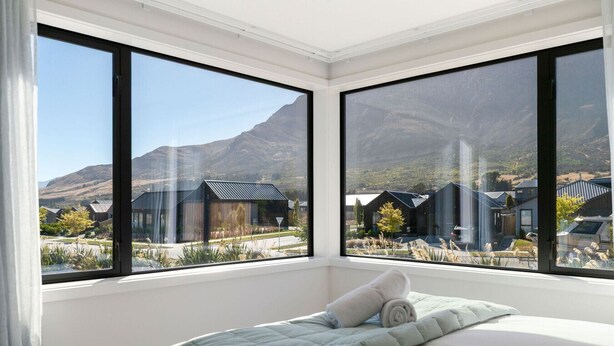 Ein Schlafzimmer mit Bett, großen Fenstern und Blick auf Häuser und Berge.