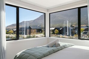 Un dormitorio con cama, ventanas amplias y vistas a casas y montañas.