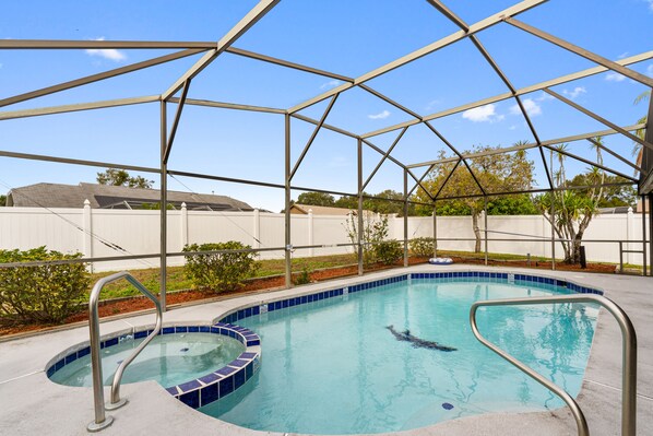 Una piscina con estructura metálica de techo, rodeada por una cerca blanca y jardines.