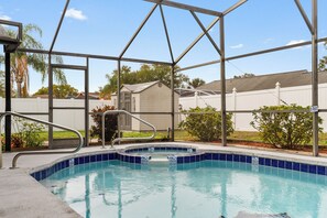 Piscina exterior con valla de seguridad metálica, rodeada de un jardín ajardinado y una cerca blanca.