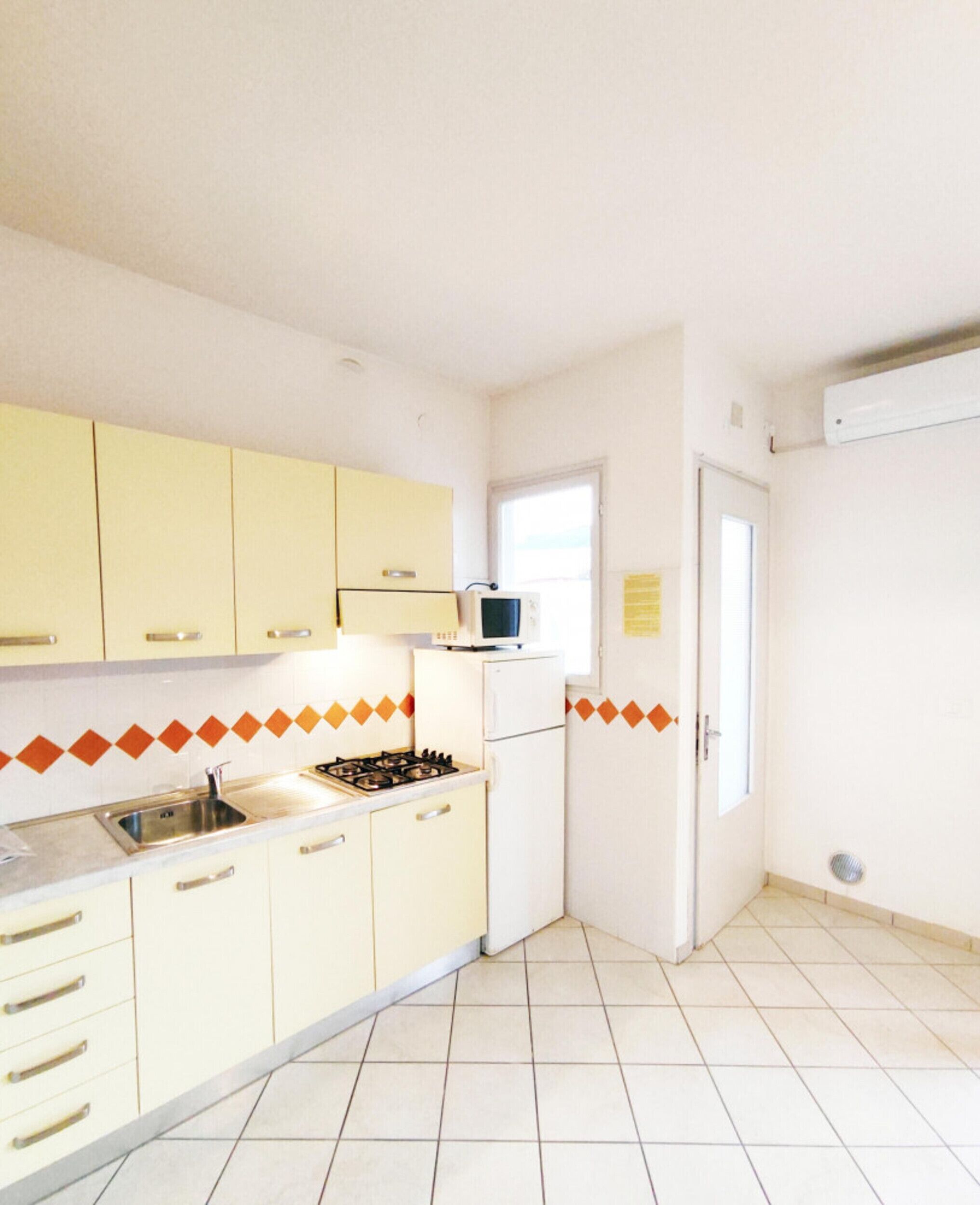 Une petite cuisine avec des meubles de couleur jaune, un réfrigérateur blanc, un four à micro-ondes et une cuisinière à gaz.