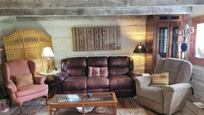 A cozy living room with a brown leather sofa, a pink armchair, and a beige armchair. A wooden coffee table is in the center, and a patterned rug covers the floor. - Red Fox Ridge Cabin Retreat - No Cleaning Fee. Relax and unwind (Butler)