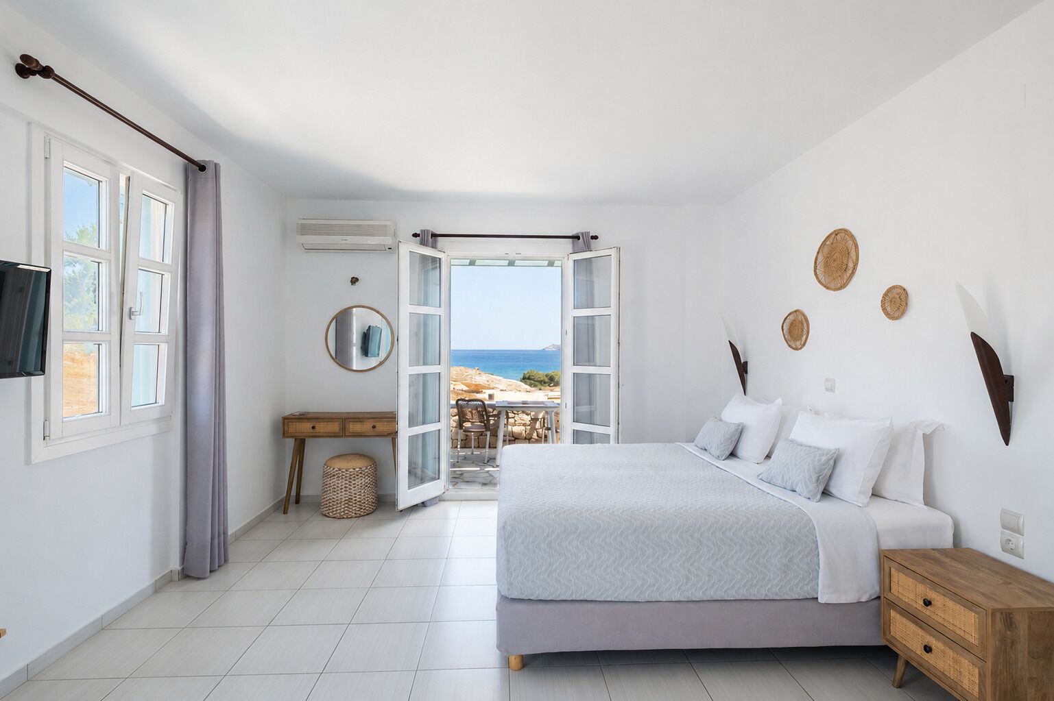 Une chambre à coucher avec un lit, une table de chevet et une vue sur la mer, visible par une porte ouverte.